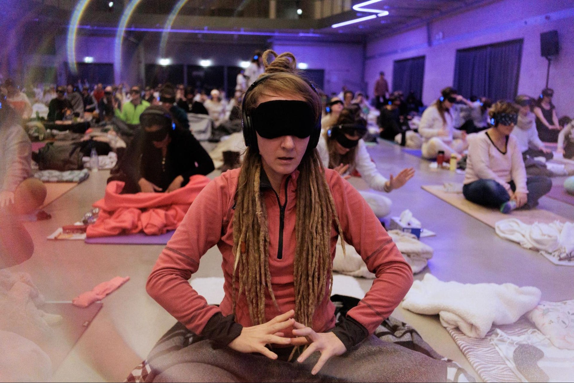 A woman wearing a blindfold and headphones sits in meditation during an immersive group breathwork session.