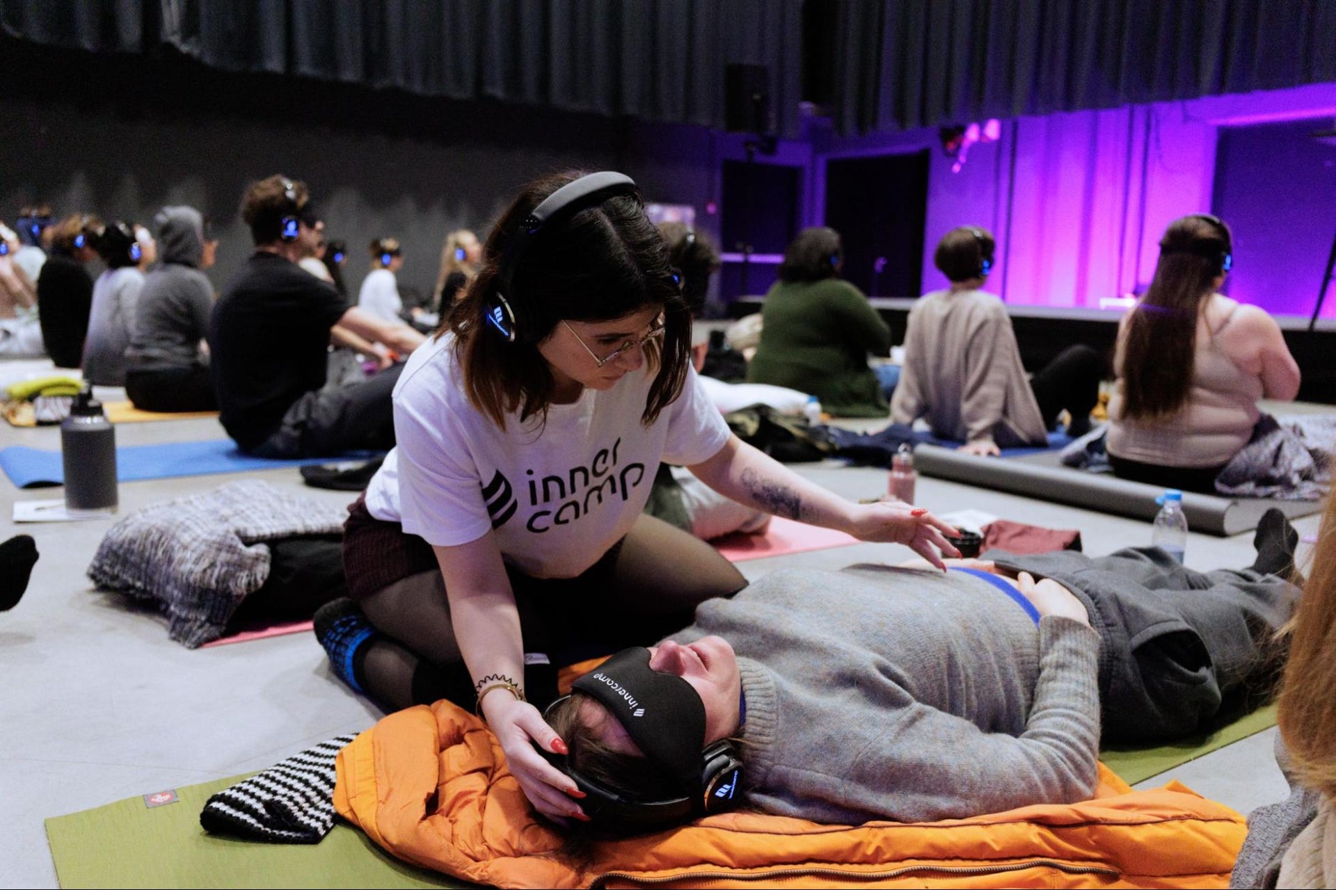 An Innercamp facilitator gently guides a lying, blindfolded participant through a breathwork practice session.