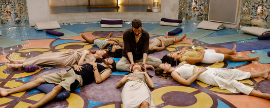 Group breathwork session with participants lying on a mandala patterned floor while a facilitator supports one breather