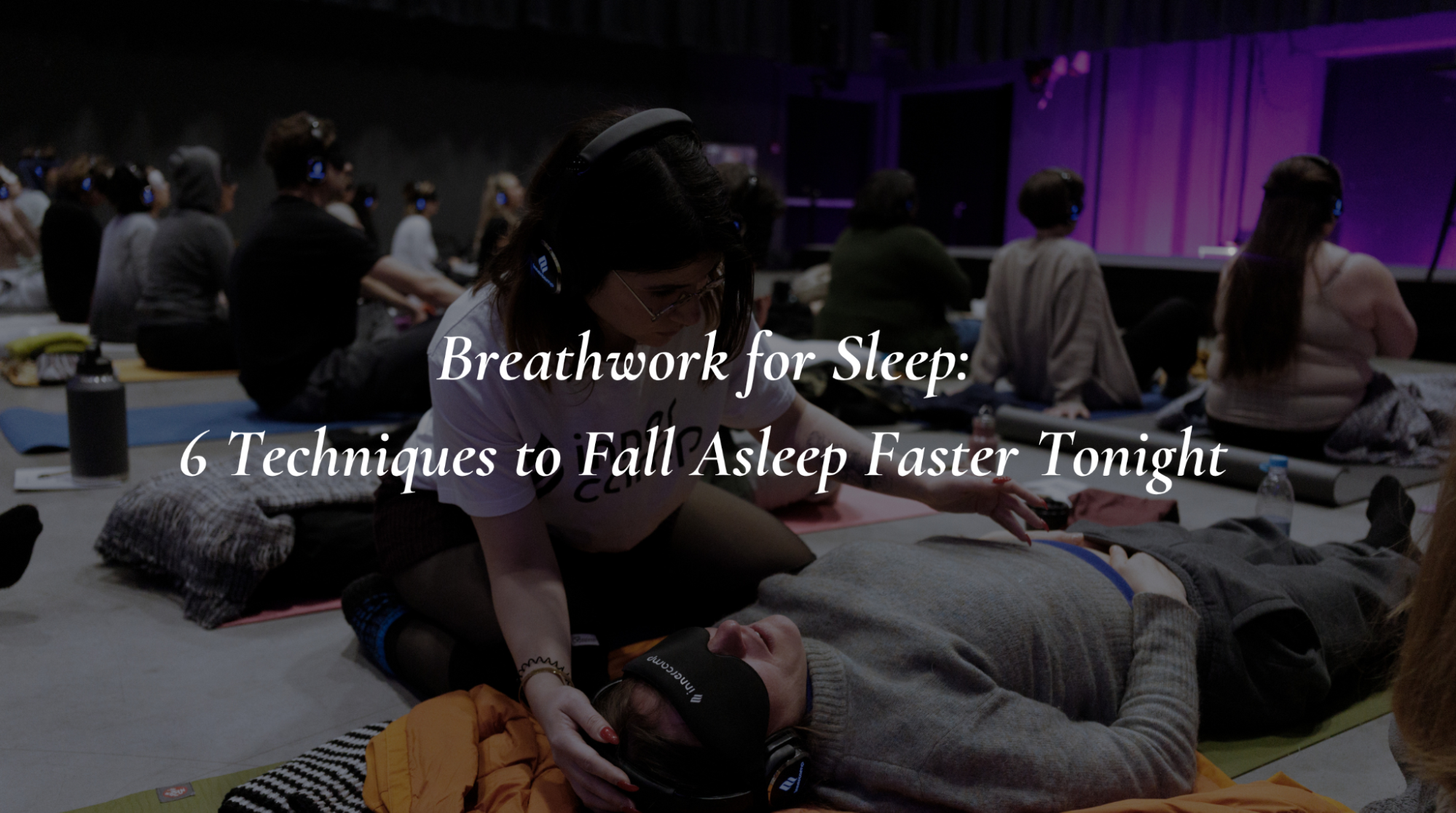 A breathwork facilitator gently guides a participant through calming relaxation techniques in a group sleep session.