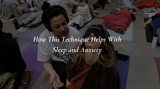 A facilitator guides a blindfolded, blanket-wrapped participant through a calming group breathwork practice.