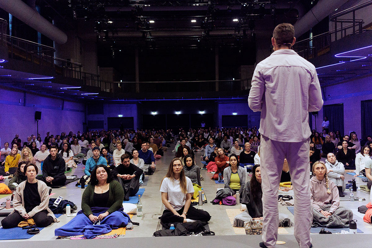 Person addressing a large audience in a dark auditorium with blue lighting.