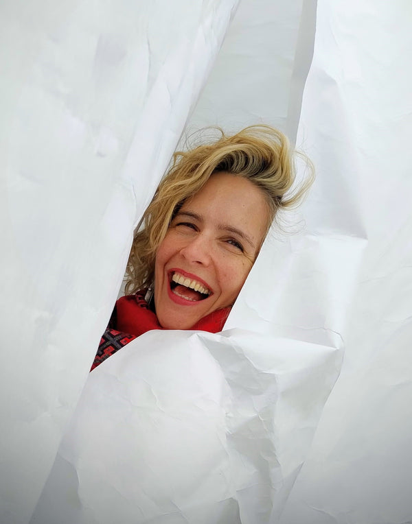 Person peeking out from behind white curtains with a joyful expression
